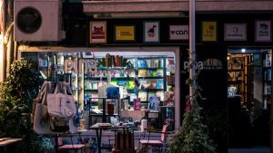 Charming nighttime bookstore and cafe scene, inviting ambiance with outdoor seating and books on display.