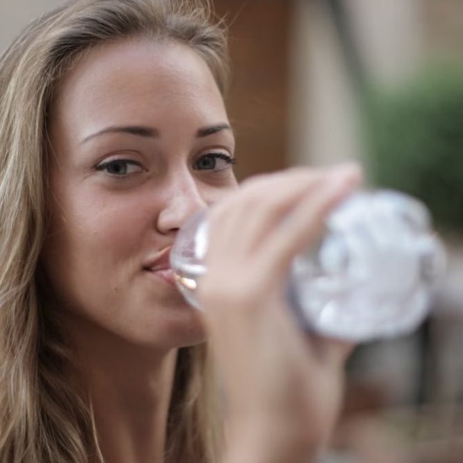 Portrait of a smiling woman drinking bottled water outdoors, enjoying hydration and relaxation.