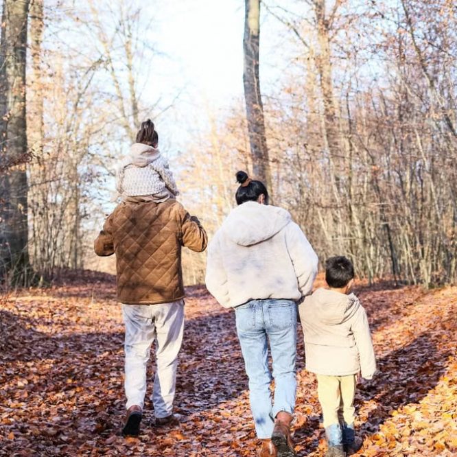 A family of four strolling on a leaf-covered path in a fall forest.